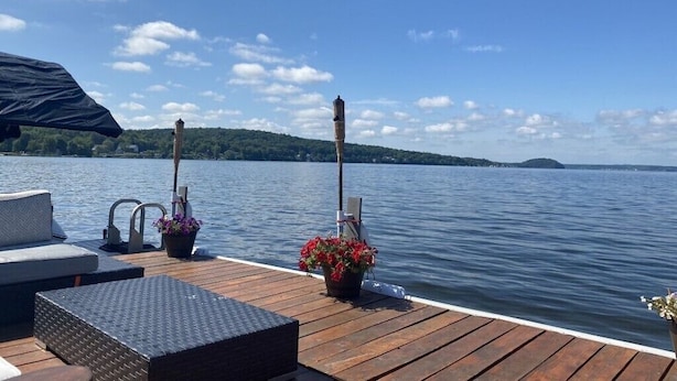 A wooden deck with outdoor seating, a covered area, and a view of a lake with distant land.
