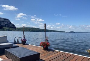 A wooden deck with outdoor seating, a covered area, and a view of a lake with distant land. - 5 Bedroom Bungalow on Beautiful Saratoga Lake (Saratoga Springs)