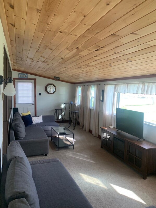 A spacious living room with a wooden ceiling, a large flat-screen TV, a sofa set, a coffee table, and a small bar area. - 5 Bedroom Bungalow on Beautiful Saratoga Lake (Saratoga Springs)