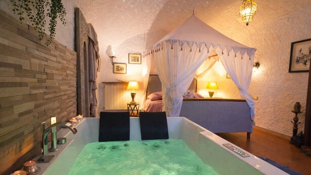 Ein Zimmer mit einer großen Badewanne, einem Himmelbett, einer Wandheizung und einem kleinen Tisch mit einer Lampe.