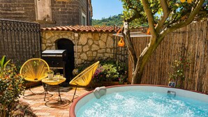 Ein Garten mit Whirlpool, zwei gelbe Stühle, einem Grill und einer Steinmauer.
