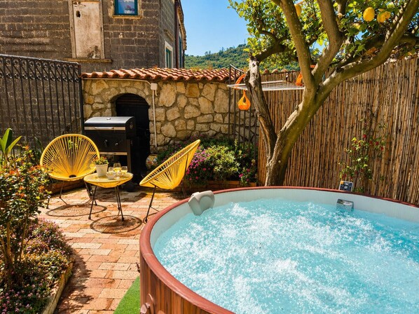 A backyard with a hot tub, two yellow chairs, a barbecue grill, and a stone wall.
