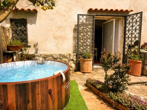 Un bain à remous en bois, situé dans un jardin agrémenté d’un mur en pierre, de plantes en pot et d’un toit recouvert de tuiles.