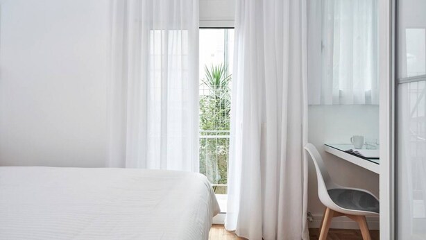 A bedroom with a bed, a desk, and a chair. There is a window with curtains, and a balcony with greenery outside. - Hilton-Ilisia Park 2Bd Elite Living (Athina)