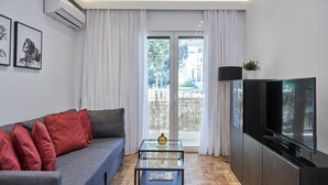 A modern living room with a sofa, a glass coffee table, a flat-screen TV, and a sliding glass door leading to an outdoor area. - Hilton-Ilisia Park 2Bd Elite Living (Athina)