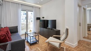 A modern living room with a sofa, a glass coffee table, a TV on a cabinet, and a chair. - Hilton-Ilisia Park 2Bd Elite Living (Athina)