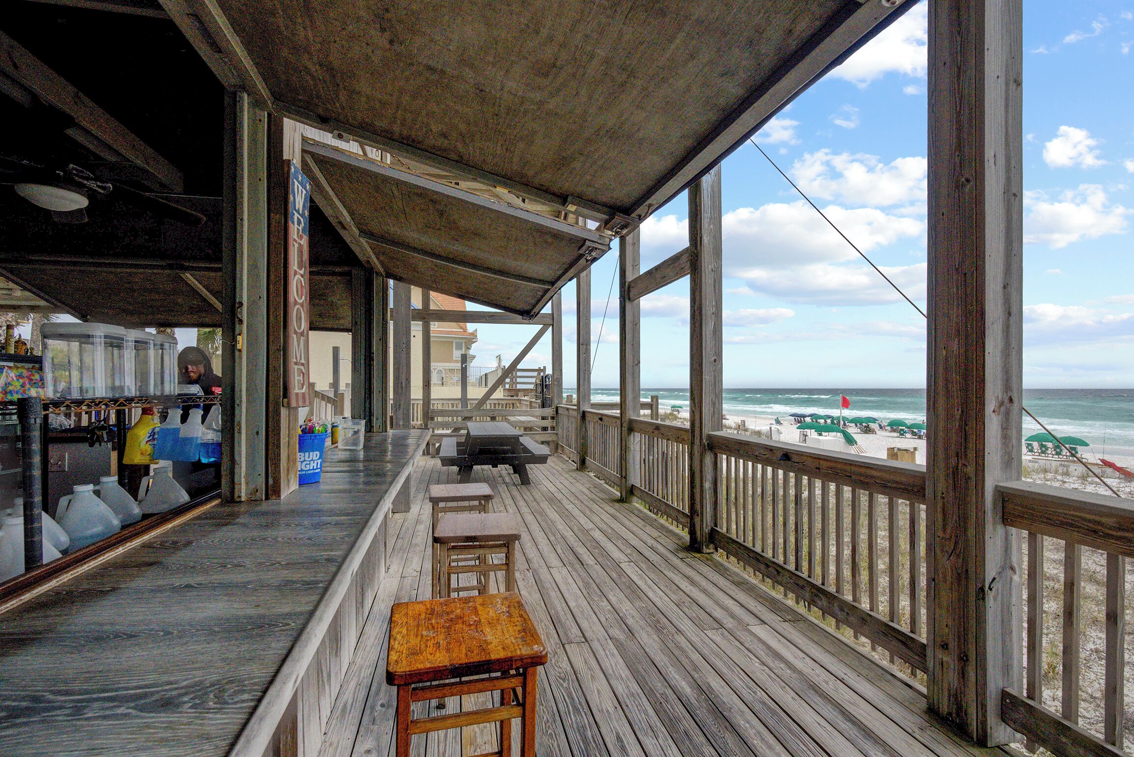A wooden deck with a view of the beach, outdoor seating, and a bar area.