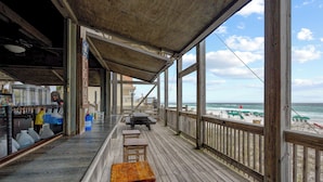 Une terrasse en bois offrant une vue sur la plage, avec des sièges extérieurs et un espace bar.
