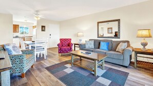 A living room with a sofa, armchair, coffee table, and a dining area with chairs and a table. - Your Tybee Island Escape – Oceanfront Condo 20C (Tybee Island)