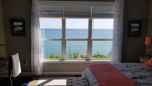 Ein Schlafzimmer mit großem Fenster und Meerblick, einem Bett mit blumigem Überwurf und einem blauen Teppich auf dem Boden.