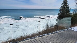 Eine Holzterrasse mit Blick auf einen verschneiten Strand, Eisformationen und einen klaren Himmel.