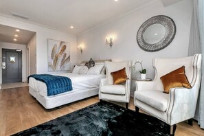 A hotel room with a bed, two armchairs, a round mirror, and a painting on the wall.