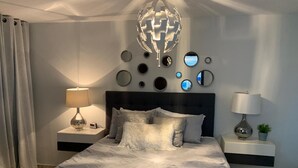 Une chambre moderne avec un grand lit, deux tables de chevet avec des lampes, un élément décoratif mural et une plante en pot.