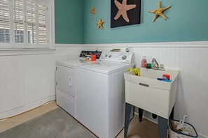A laundry room with a front-loading washer and dryer, a small sink with a trash can, and decorative starfish on the wall.