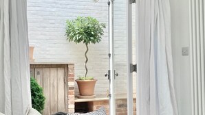 A room with a sliding glass door leading to a patio area with a potted plant and a brick wall. - Sea air and starry nights - there's space for two and your four legged friend. (Cromer)
