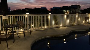 Zona junto a la piscina con valla blanca, sillas y una mesa.