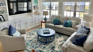 Una sala de estar con un televisor de pantalla plana grande, un sofá color beige, una mesa de centro azul y un tapete estampado.