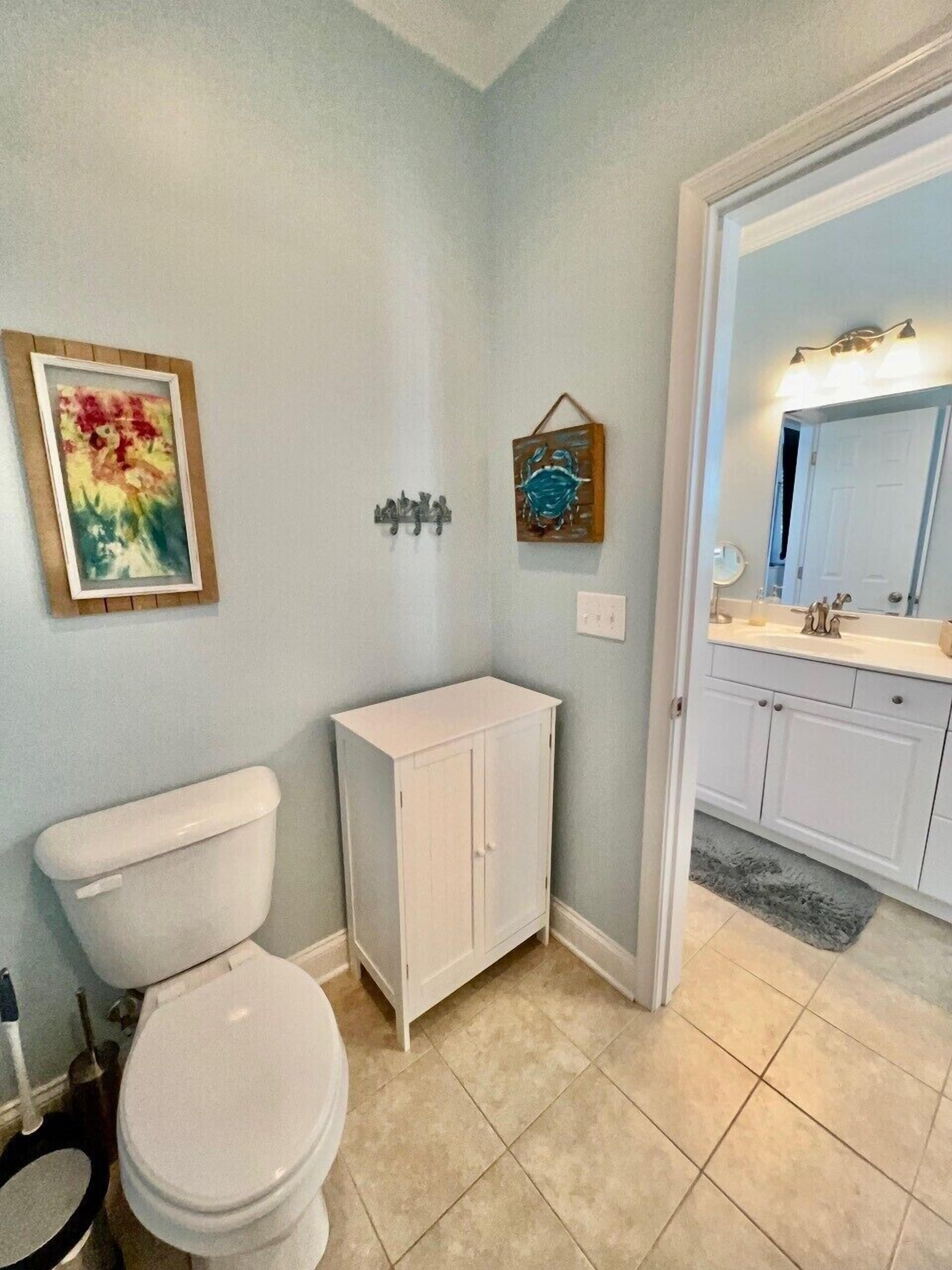 A bathroom with a toilet, a cabinet, a sink with a mirror, and a framed painting on the wall.