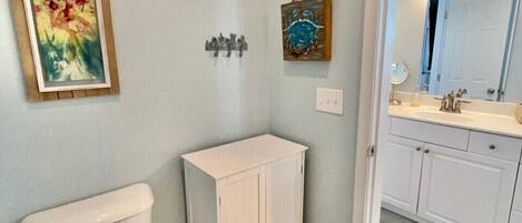 A bathroom with a toilet, a cabinet, a sink with a mirror, and a framed painting on the wall.
