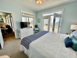 A bedroom with a large bed, a dresser, a television, and a window.