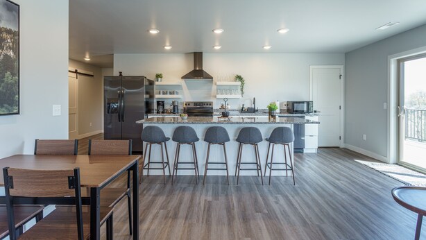 Een moderne keuken met een centraal eiland, barstoelen en een eettafel met stoelen.