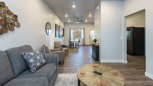 A spacious living room with a gray sofa, a coffee table, and a dining area in the background. - The Lower Hillsview Loft (Spearfish)
