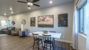 A modern living room with a dining area, wooden flooring, a ceiling fan, and artwork on the walls. - The Lower Hillsview Loft (Spearfish)