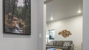 A modern living room with a grey sofa, a coffee table, and a wall-mounted abstract art piece. - The Lower Hillsview Loft (Spearfish)
