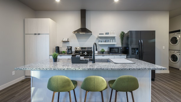 A modern kitchen with a central island, bar stools, a built-in oven, microwave, and a stainless steel refrigerator. - The Lower Hillsview Loft (Spearfish)