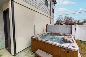 Een hottub met een houten buitenkant en een bankje, gelegen in een achtertuin met een huis op de achtergrond.