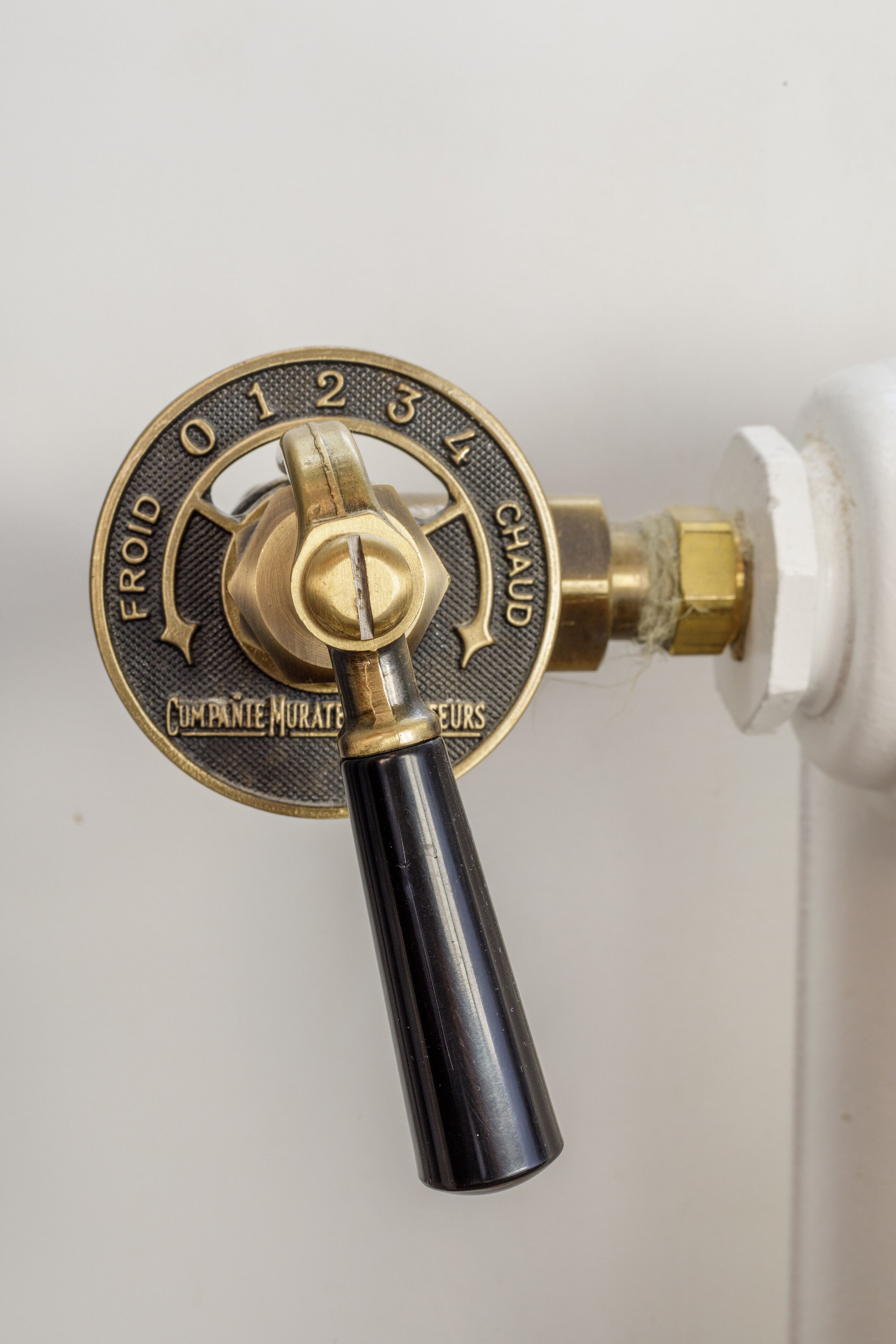 Une serrure en laiton avec un bouton noir, un mur blanc et un robinet en laiton.