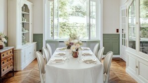 A dining room with a white table set for six, large windows, and a view of greenery outside. - L'Hôtel Particulier (Asnieres-sur-Seine)