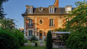 A large, historic building with a symmetrical facade, a central entrance, and a small garden area with outdoor seating. - L'Hôtel Particulier (Asnieres-sur-Seine)
