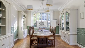 A dining room with a large wooden table, white cabinetry, and a view of the garden through a large window. - L'Hôtel Particulier (Asnieres-sur-Seine)