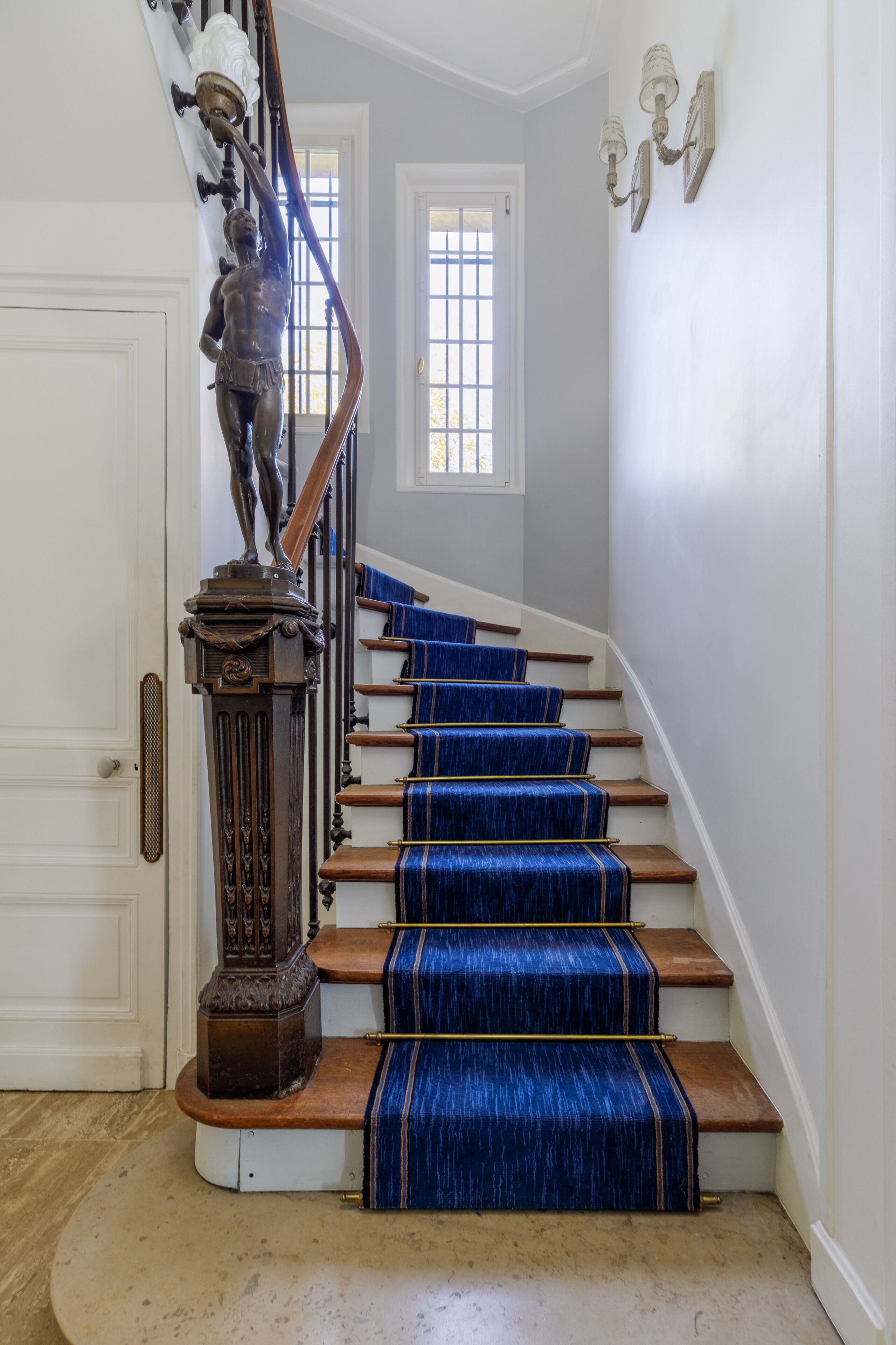 A staircase with blue carpeted steps and a wooden handrail, leading to a door.