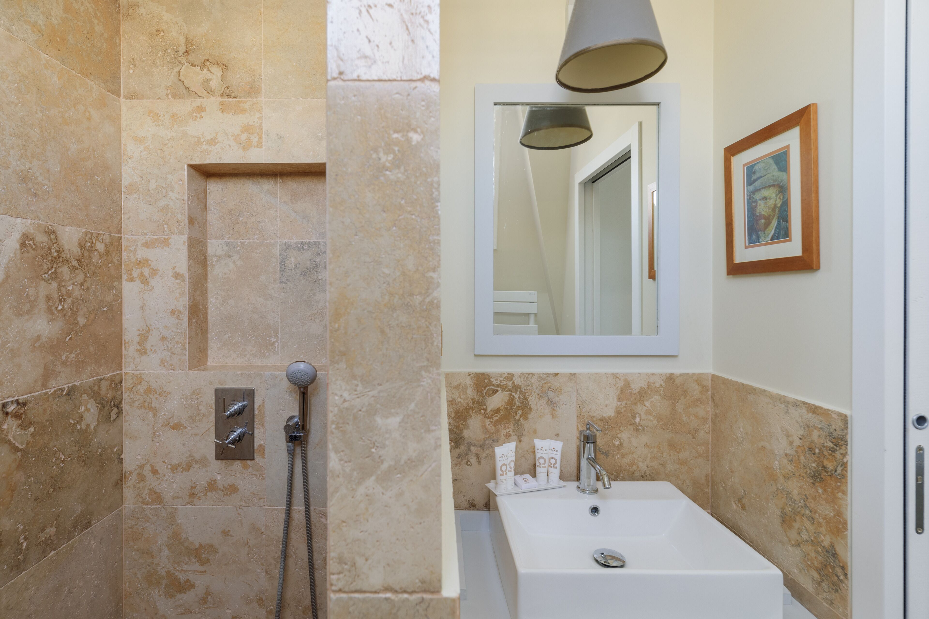Une salle de bain avec des carreaux de couleur beige, un lavabo blanc, un miroir et un tableau encadré au mur.