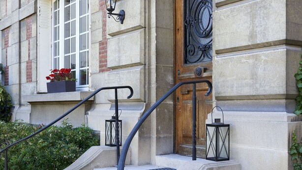 A stone building with a wooden door, a set of stone steps, and two lantern-style lights on the wall. - L'Hôtel Particulier (Asnieres-sur-Seine)