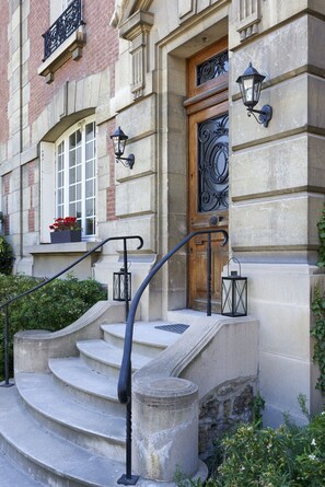 Un bâtiment en pierre avec une porte en bois, un escalier en pierre et deux lampes murales de style lanterne.