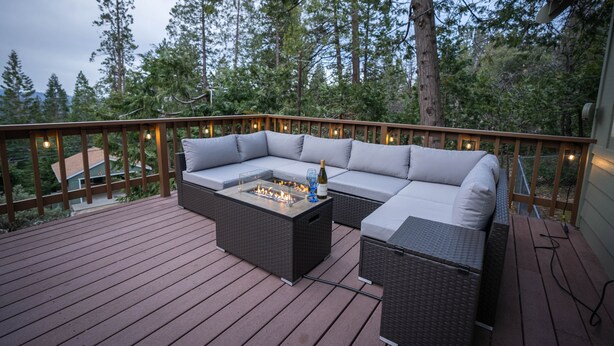 Une terrasse dotée d’un canapé modulable et d’un foyer, entourée d’une rambarde en bois et illuminée de guirlandes lumineuses.