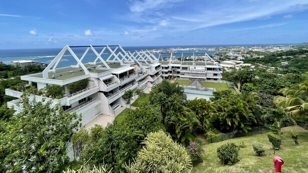Un edificio moderno con una estructura de techo triangular distintiva, rodeado de vegetación exuberante y una vista despejada del océano.