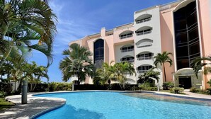 Una piscina rodeada de palmeras y un edificio de varios pisos con balcones.