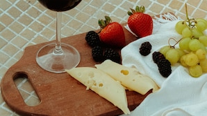 Une planche en bois sur laquelle on a disposé un verre de vin rouge, du fromage, des fraises, des mûres et des raisins, le tout posé sur une nappe à carreaux.