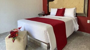 Une chambre d’hôtel avec un lit, une table de chevet, une petite table et une chaise, le tout agrémenté d’un bouquet de fleurs.