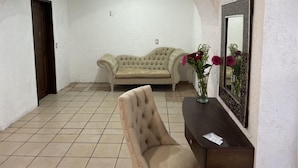Une pièce avec un canapé beige, un fauteuil, une petite table d’appoint en bois foncé et un miroir au mur.