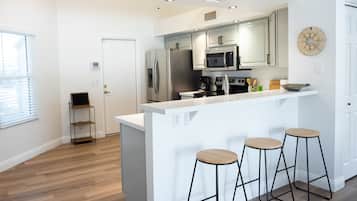 A modern kitchen with white cabinetry, stainless steel appliances, and a central island with stools.