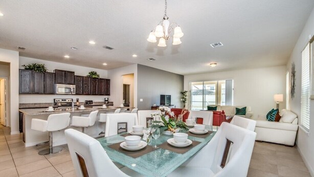 A modern kitchen with white cabinetry, a central island with bar seating, and a dining area with a glass-top table. - 6 bedroom 5 bathroom with Spa and Games Room Brand New Modern Furnishings (Davenport)