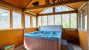 A wooden cabin with a hot tub, large windows, and a bear silhouette on the ceiling.
