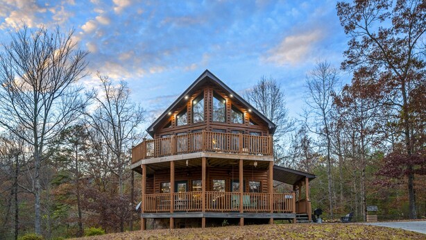 A two-story log cabin with a balcony, surrounded by trees.