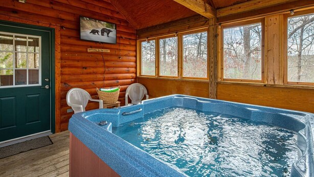 A cabin interior with a hot tub, wooden walls, a welcome sign, and two chairs by the door.