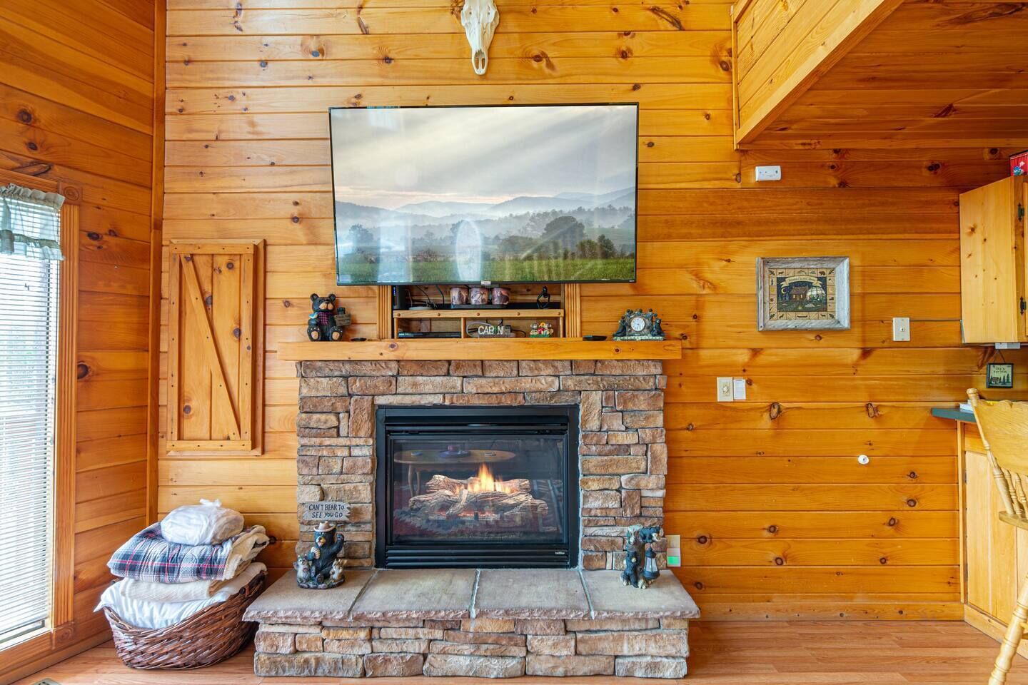 Ein gemütliches Blockhaus-Interieur mit Kamin aus Stein, Holzwänden, einem angebrachten Fernseher und einem gerahmten Bild über dem Kamin.